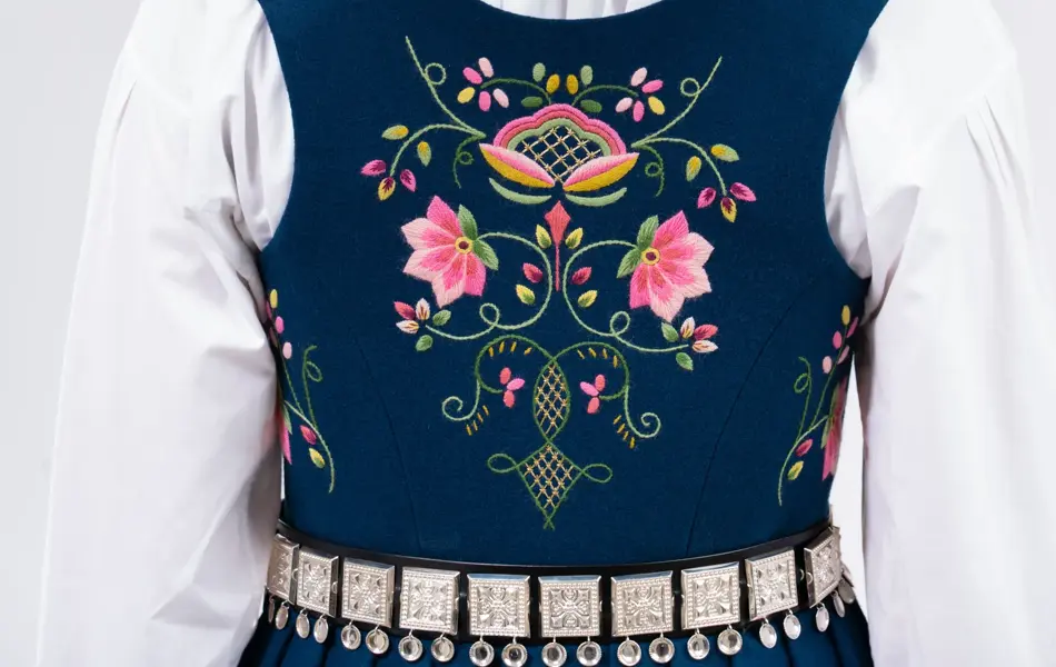 Jente som viser baksiden av en blå bunad med lue