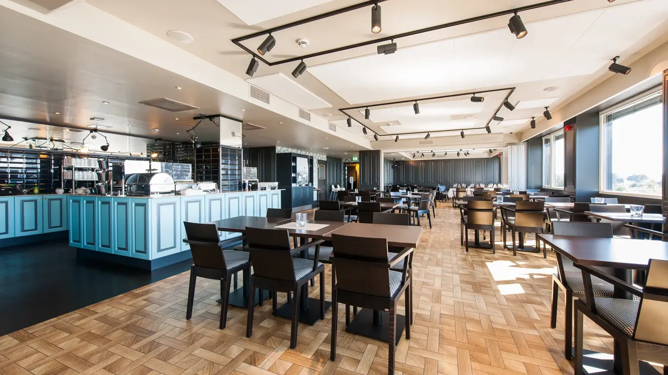 Spiseområde, brune bord og stoler, vindu, hvitt tak, lyse vegger.