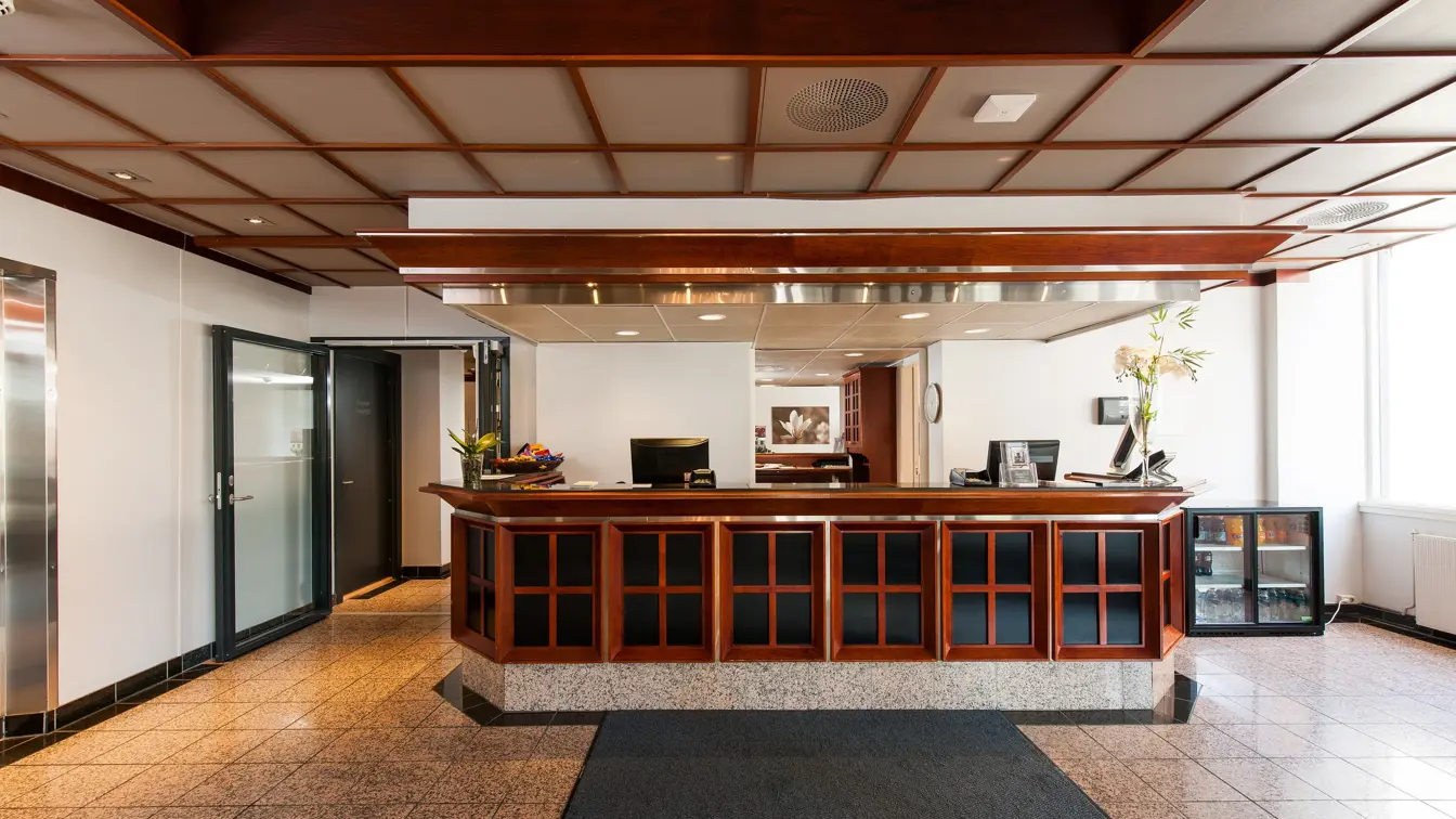 Resepsjonsdisk, beige gulvfliser, vindu, heis