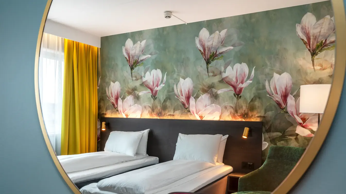 Blomstertapetvegg, to enkeltsenger, rosa stol, speil på veggen, vindu, gule gardiner