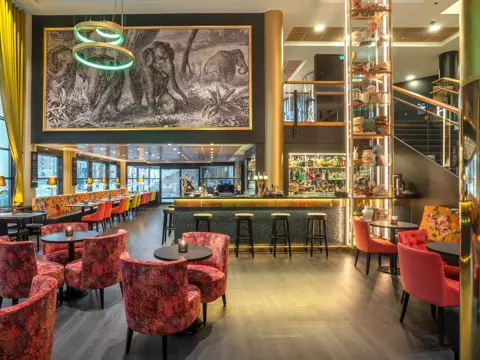 Bar, diverse sittegrupper, rosa stoler, svarte bord. 