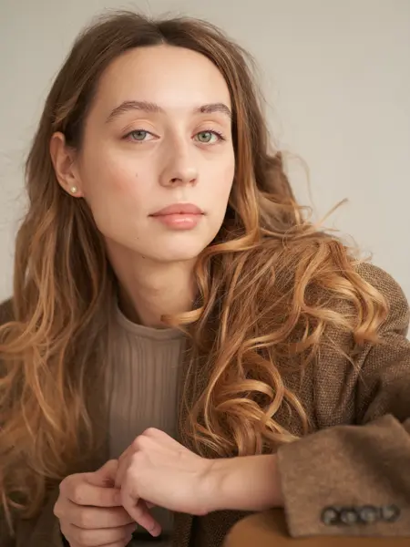 Nærbilde av dame i sjokoladebrun kåpe og lys brun genser poserer for kamera 