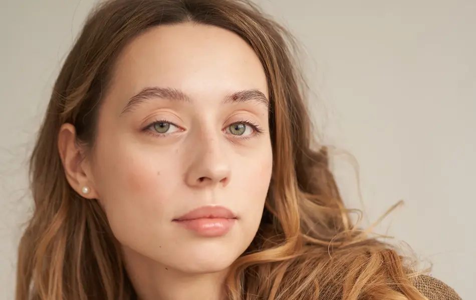 Nærbilde av dame i sjokoladebrun kåpe og lys brun genser poserer for kamera 