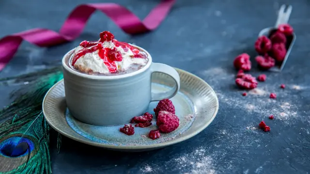 Kakao med bringebær og krem i en kopp som er plassert på en tallerken