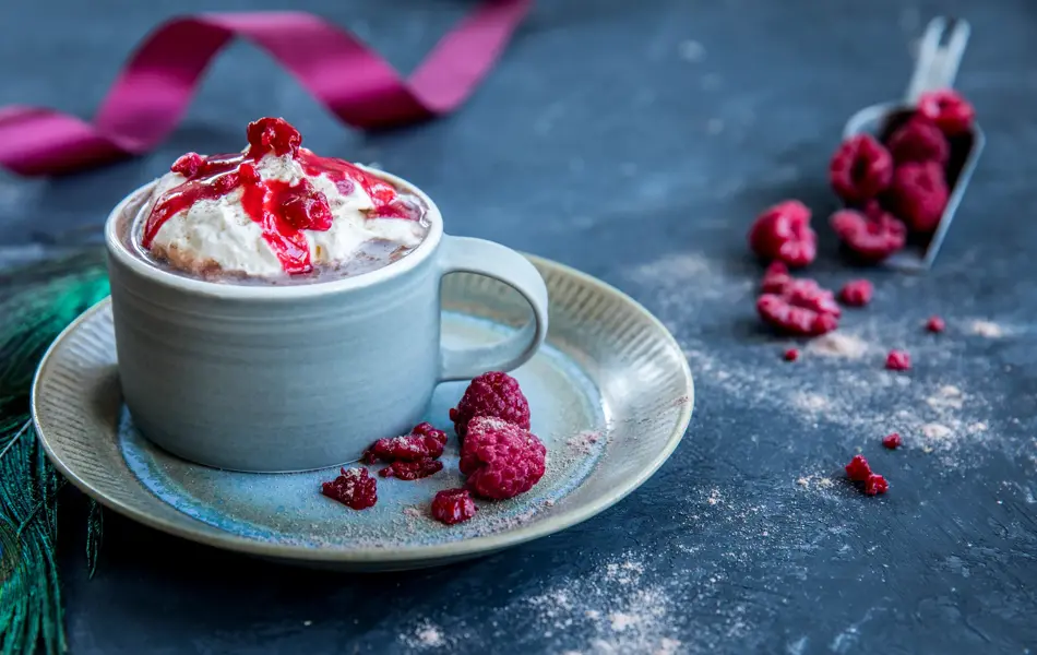 Kakao med bringebær og krem i en kopp som er plassert på en tallerken