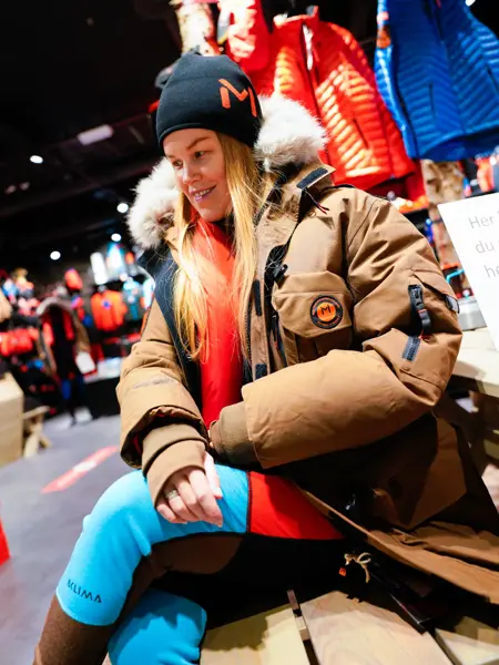 Jente med orangesekk og blådunjakke, og langrennski og slalåmski