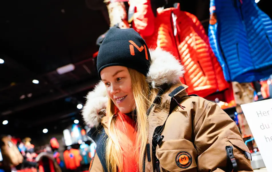 Jente med orangesekk og blådunjakke, og langrennski og slalåmski