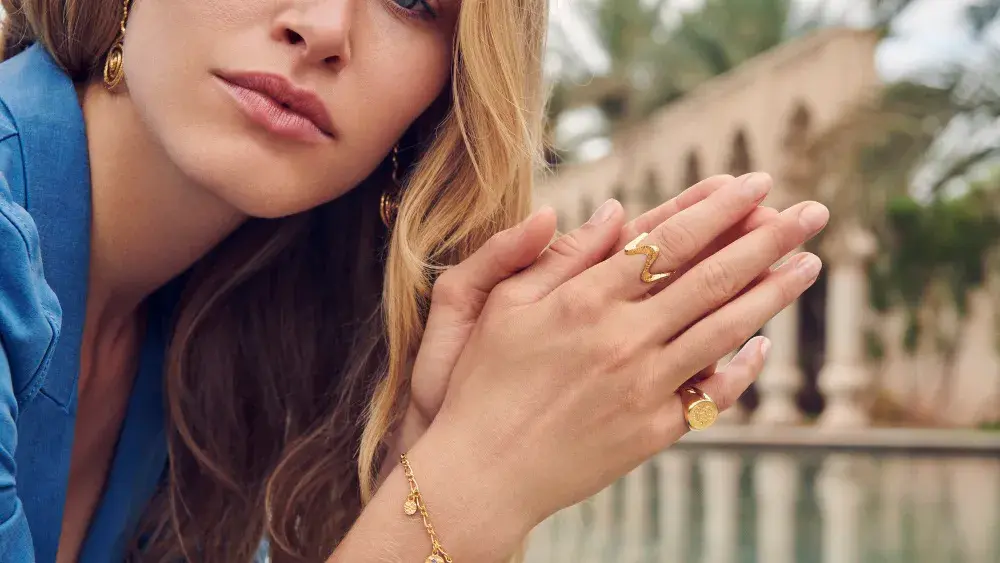 Dame holder hendene foran seg med ringer og armbånd i gull