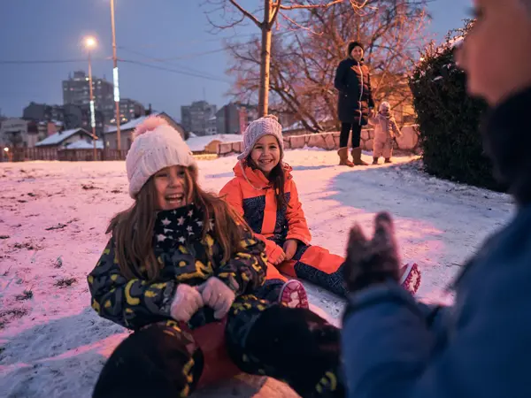 Excited and playful children having fun while sliding wth a slide during a winter day in the sunset