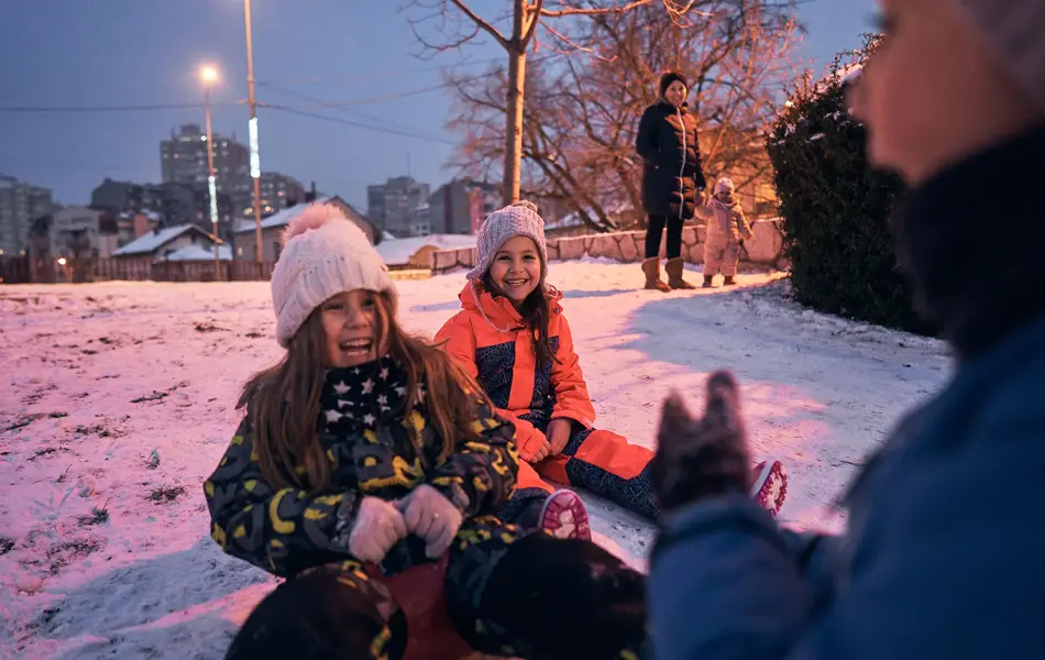 Excited and playful children having fun while sliding wth a slide during a winter day in the sunset