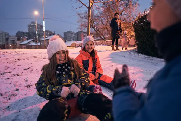 Excited and playful children having fun while sliding wth a slide during a winter day in the sunset