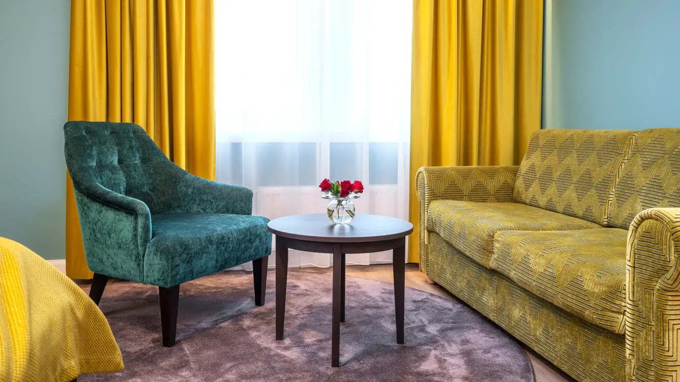 Stort vindu med gule gardiner fra tak til gulv. Limegrønn sofa, turkise vegger, sort rundt bord og turkis lenestol. I superior rom på Thon Hotel Høyers i Skien.