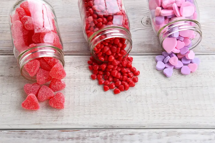 Canning jars laying on their sides filled with candy hearts and for Valentine's Day  on a rustic wood table.
