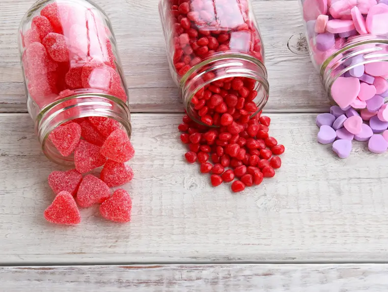 Canning jars laying on their sides filled with candy hearts and for Valentine's Day  on a rustic wood table.