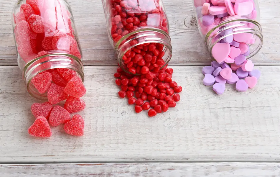 Canning jars laying on their sides filled with candy hearts and for Valentine's Day  on a rustic wood table.