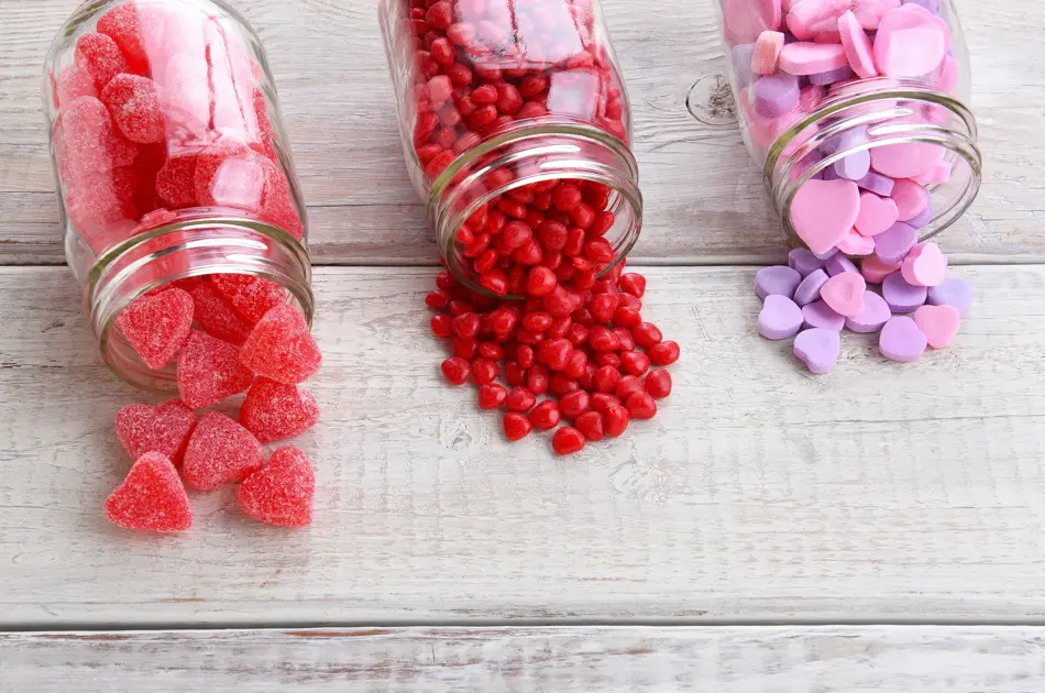 Canning jars laying on their sides filled with candy hearts and for Valentine's Day  on a rustic wood table.