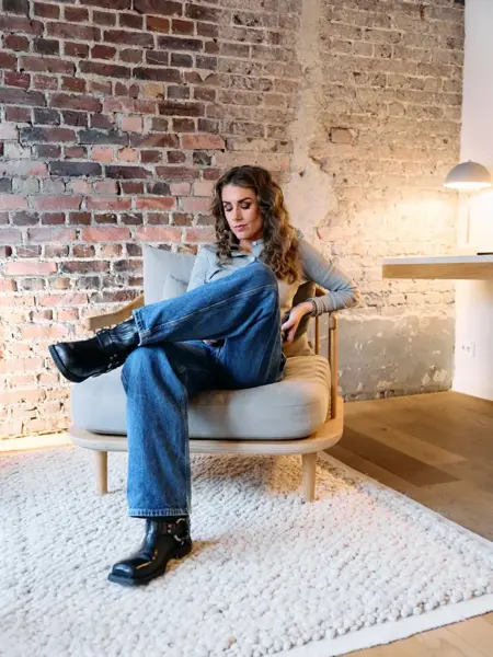 Tone sitter i en stol med jeans, topp og sorte boots.