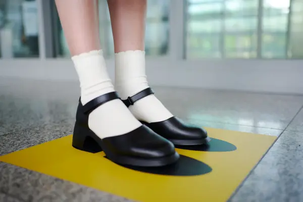 Dame med Mary Janes og hvite sokker som står på en gul firkant