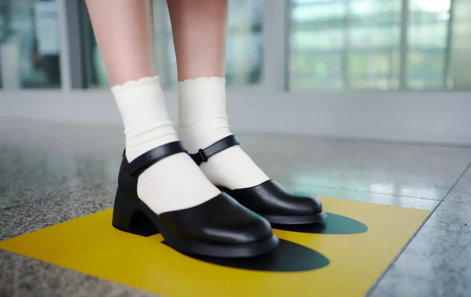 Dame med Mary Janes og hvite sokker som står på en gul firkant