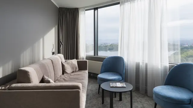 Business rom med sofa langs veggen, sofabord, to blå stoler og store vinduer med utsikt