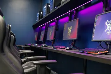 PC-skjermer på en rekke i et rom med lille LED-lys på veggen bak. Foto.