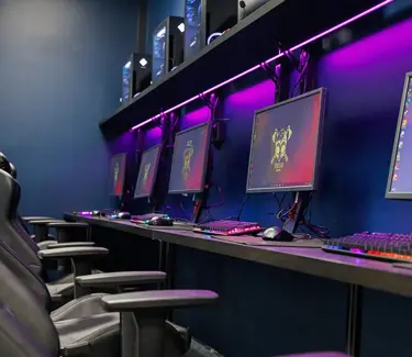 PC-skjermer på en rekke i et rom med lille LED-lys på veggen bak. Foto.