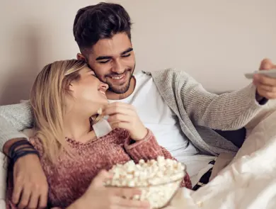 Blond jente holder skål med popkorn og lener seg på mørkhåret gutt som holder fjernkontroll