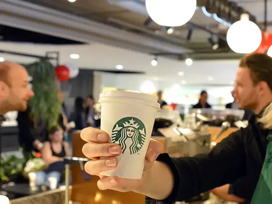 Blonde dame barista som smiler med en hvit papir kopp i hånden