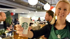 Blonde dame barista som smiler med en hvit papir kopp i hånden
