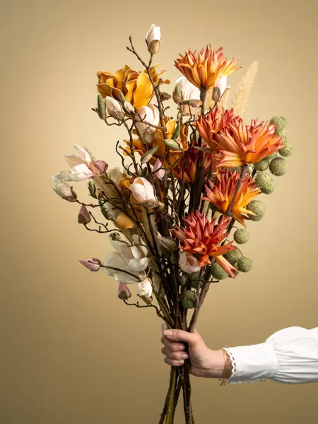 En dame som holder på med oppussing og tips om interiør trender for våren 2021. Damen har lyst halvlangt hå og har på seg en blå olaskjorte og blå olabukse. Fargene går i brunt og beige jordtoner og det er mye lilla og pastellfarger