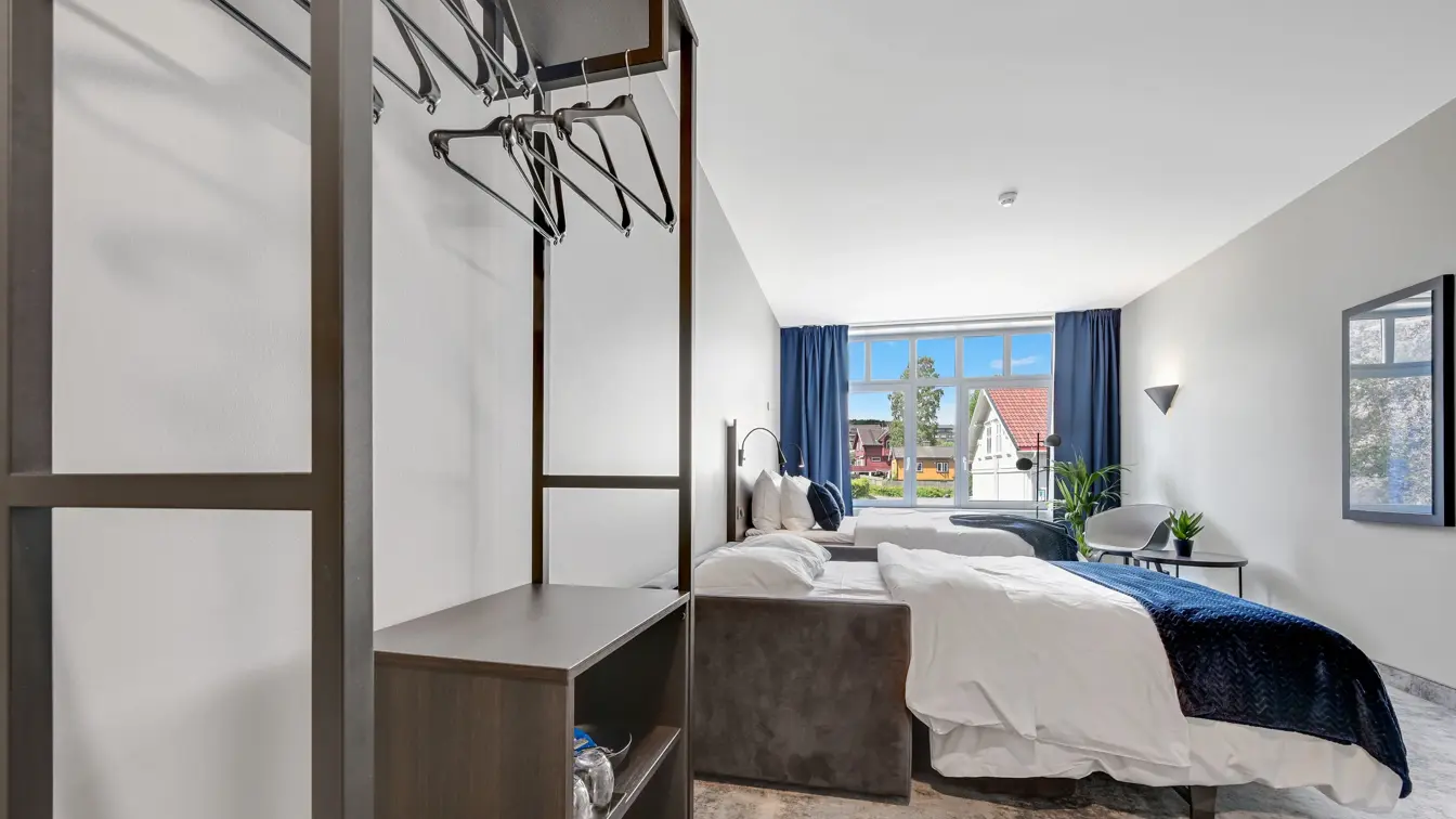 Dobbeltseng, hvite vegger, vindu, blå gardiner, skap