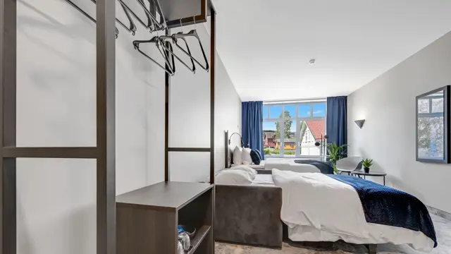 Dobbeltseng, hvite vegger, vindu, blå gardiner, skap