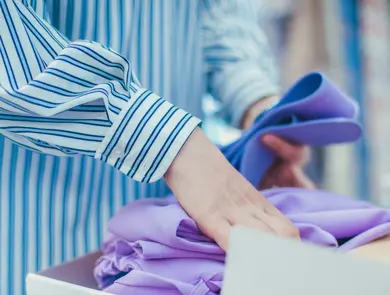 Closeup view of woman's hands folding purple clothing in the box.