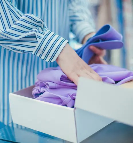 Closeup view of woman's hands folding purple clothing in the box.