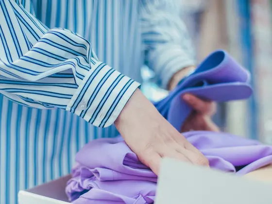 Closeup view of woman's hands folding purple clothing in the box.