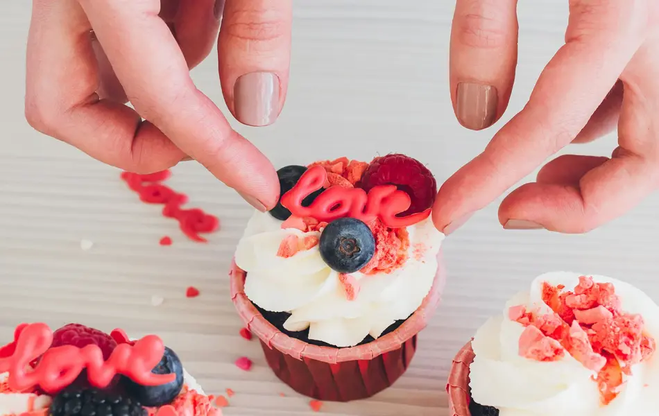 Sjokolademuffins med lys glasur dekorert med bær og spiselig love