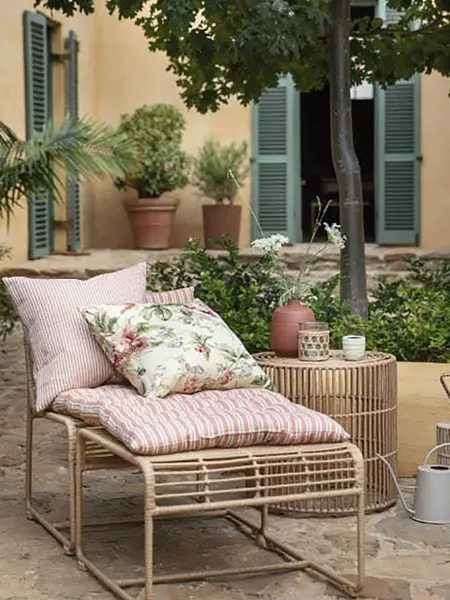 Rotting stol med krakk med rosa puter i en bakgård med mange grønne planter