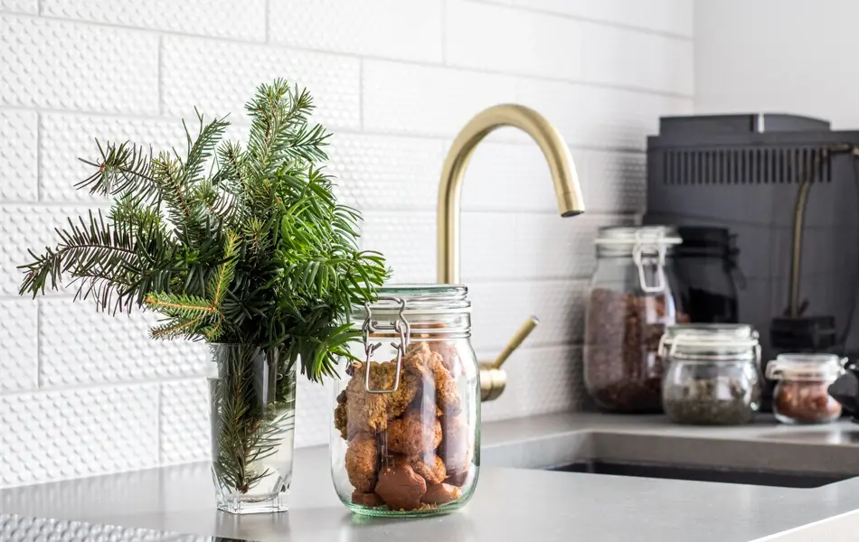 Krukker med mat i og glass med urter foran kjøkken med gullvask