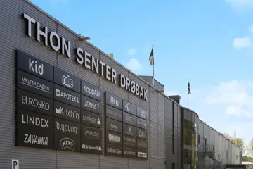 Thon Senter Drøbak fasade, med logo og navn på senteret med butikklogoer under på vegg.