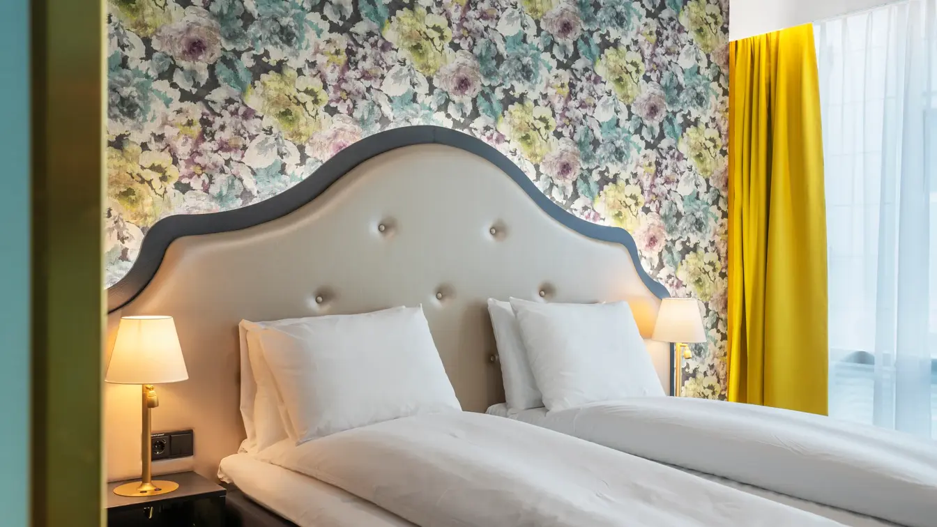 Dobbeltseng med sengegavl, blomstrete tapet og gule gardiner i dobbeltrom på Thon Hotel Cecil