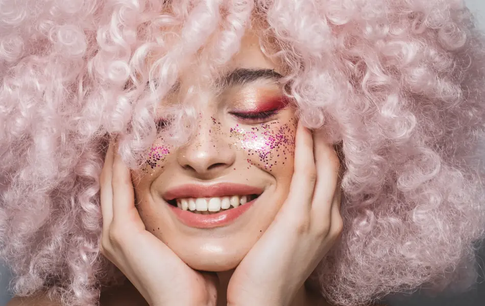 Close up studio shot of a beautiful girl wearing curly pink wig and bold make up.