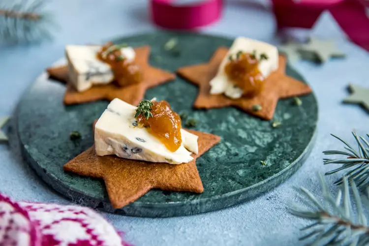Stjerneformede pepperkaker på et fat med blåmuggost og syltetøy på toppen