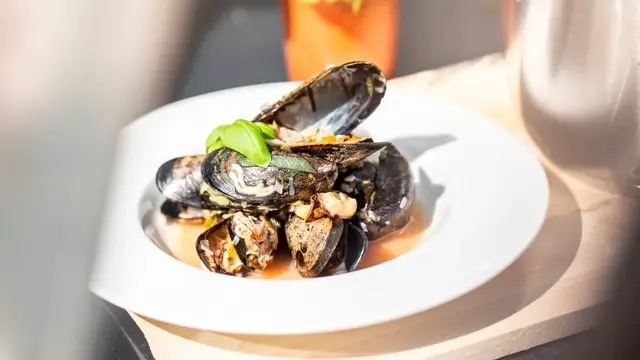 Blåskjell i gryte og i en tallerken med basilikum i bakgrunnen