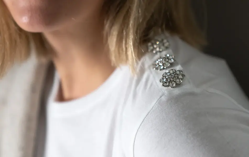 Nærbilde av damemodell med hvit topp med glitrende knapper på skulder