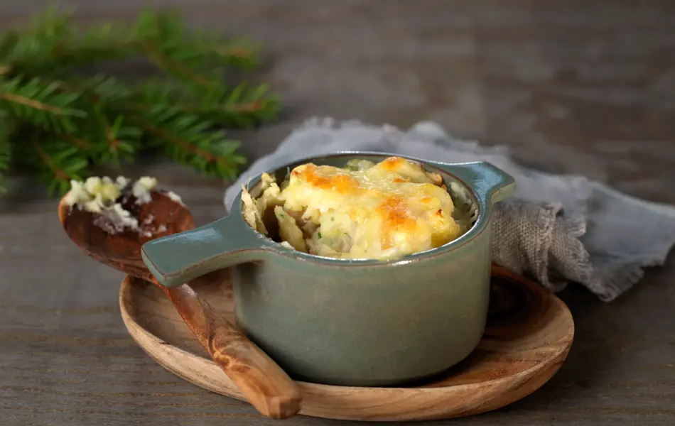 Ildfast grå porsjonsform med gratinert ost på et trebrett med en tresleiv ved siden