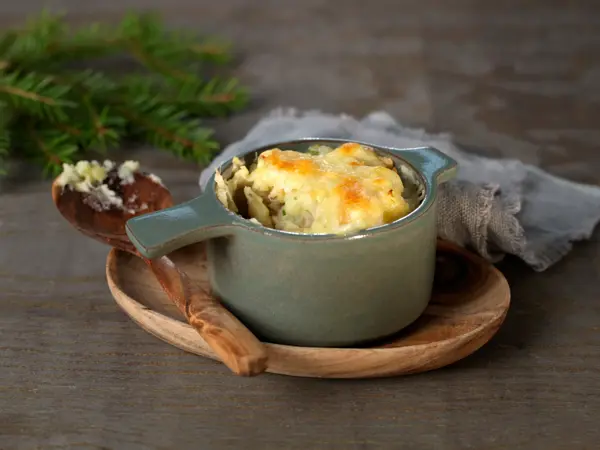 Ildfast grå porsjonsform med gratinert ost på et trebrett med en tresleiv ved siden