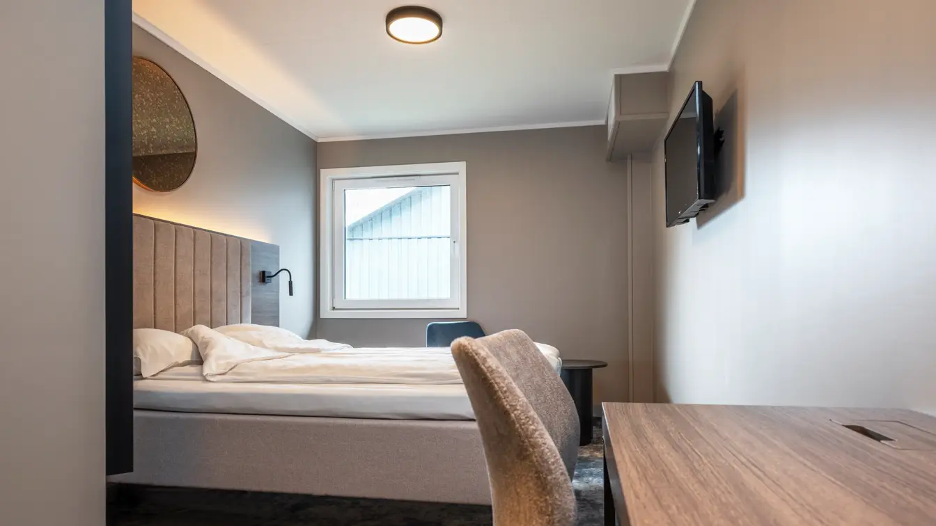 Dobbeltrom med queen seng, vegghengt TV, teppegulv og skrivebord med stol. 