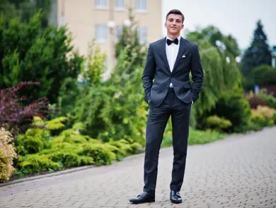Portrait of a handsome young man in formal fancy suit posing on the pavement in the park on a prom day.