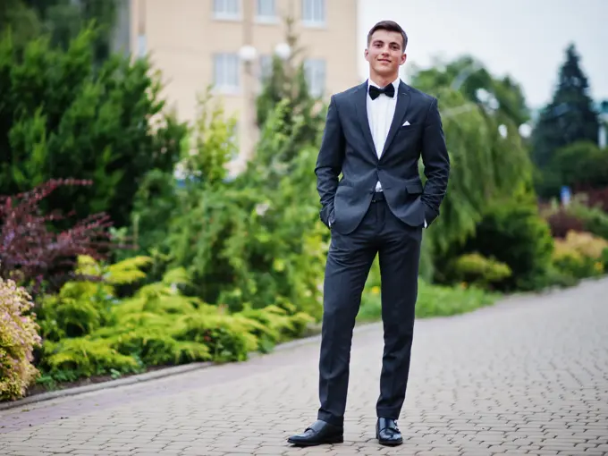 Portrait of a handsome young man in formal fancy suit posing on the pavement in the park on a prom day.