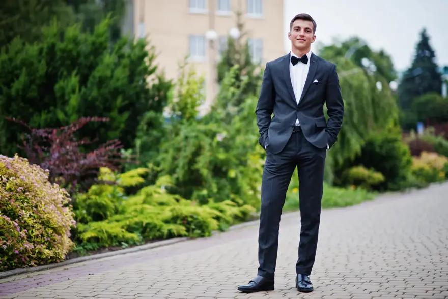 Portrait of a handsome young man in formal fancy suit posing on the pavement in the park on a prom day.